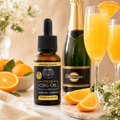 Bottle of CBG oil with a mimosa flavor, champagne bottle, and glasses with orange juice on a table.