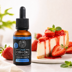 Bottle of 'Our Life' Calm CBN Oil next to a slice of strawberry cheesecake on a white surface.