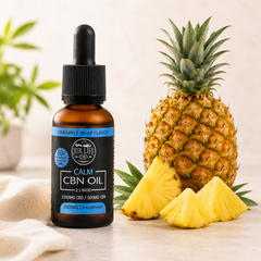 An amber glass dropper bottle of NUR LIFE CBD CALM CBN OIL in Pineapple Whisk Flavor, styled next to a whole pineapple and three pineapple slices on a light beige surface with a soft neutral background.